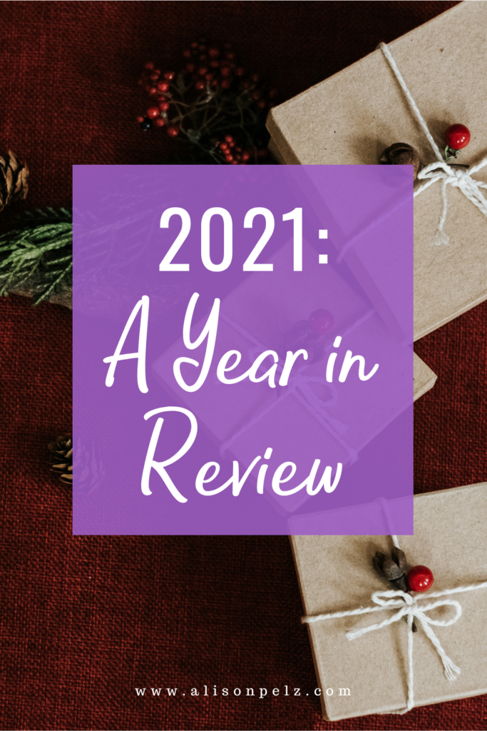 A graphic that reads "2021: A Year In Review" over a stock photo of some pine branches and gifts wrapped in brown paper, on a red background.