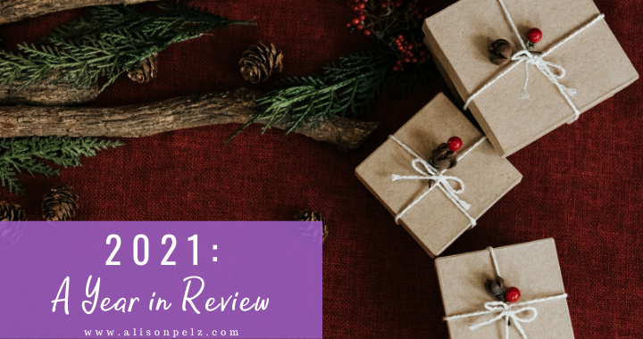 A graphic that reads "2021: A Year In Review" over a stock photo of some pine branches and gifts wrapped in brown paper, on a red background.